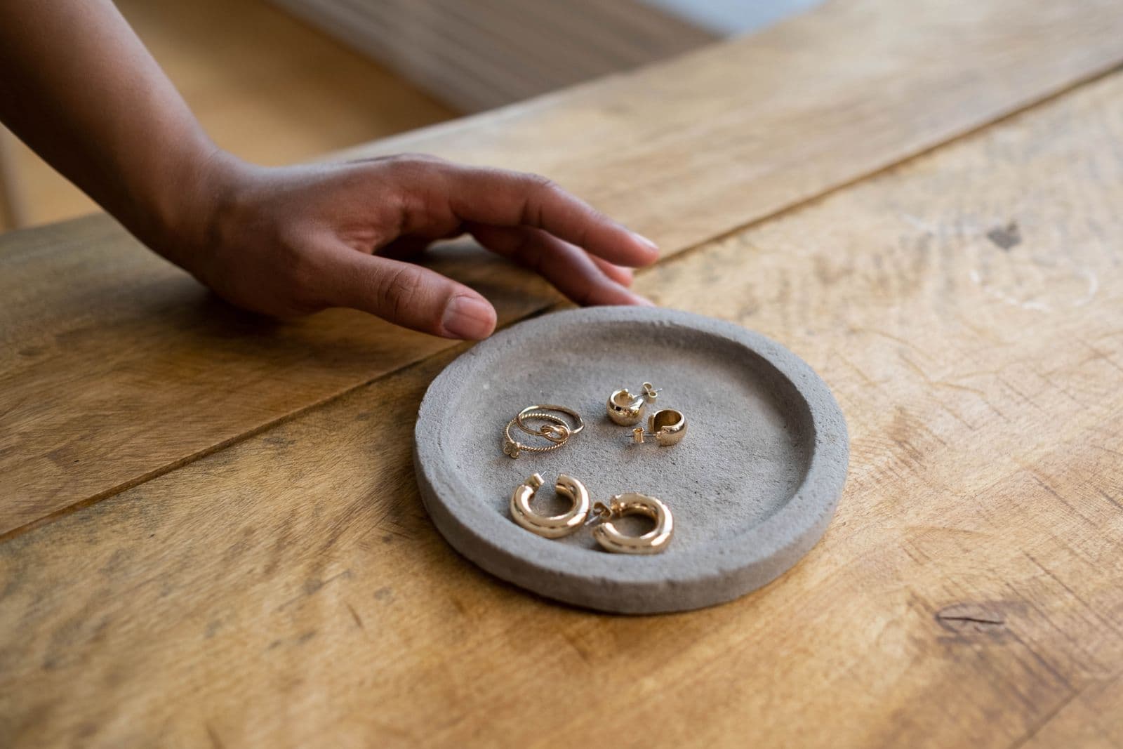 A hand reaching toward gold jewelry in the Aurelia atelier